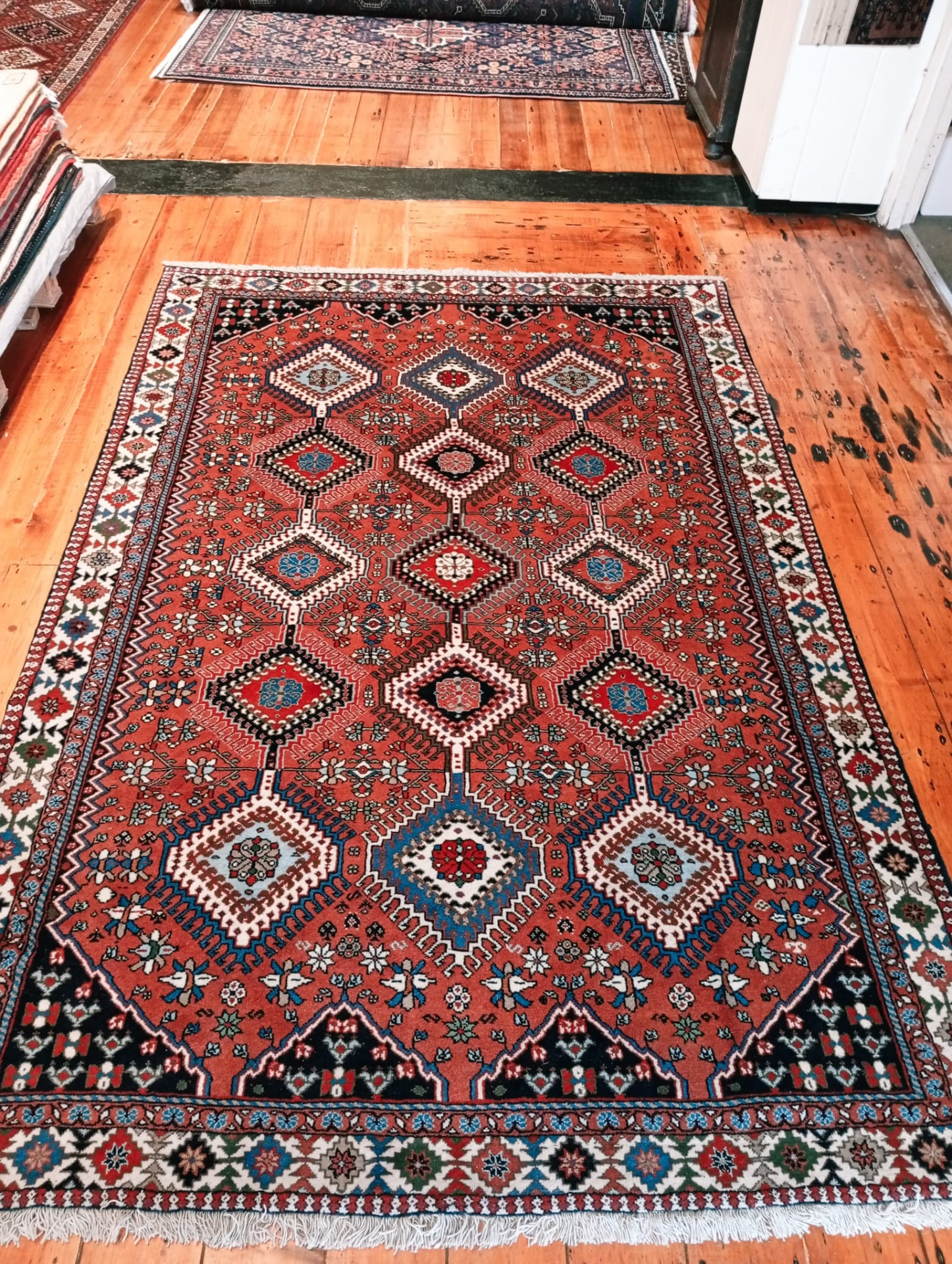 Yalameh Persian rug with terracotta field and diamond lattice, photographed on gallery floorboards